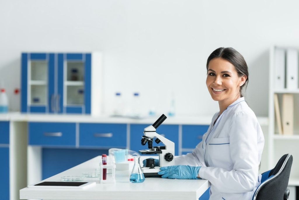 Scientist smiling at camera near digital tablet and medical equipment in lab